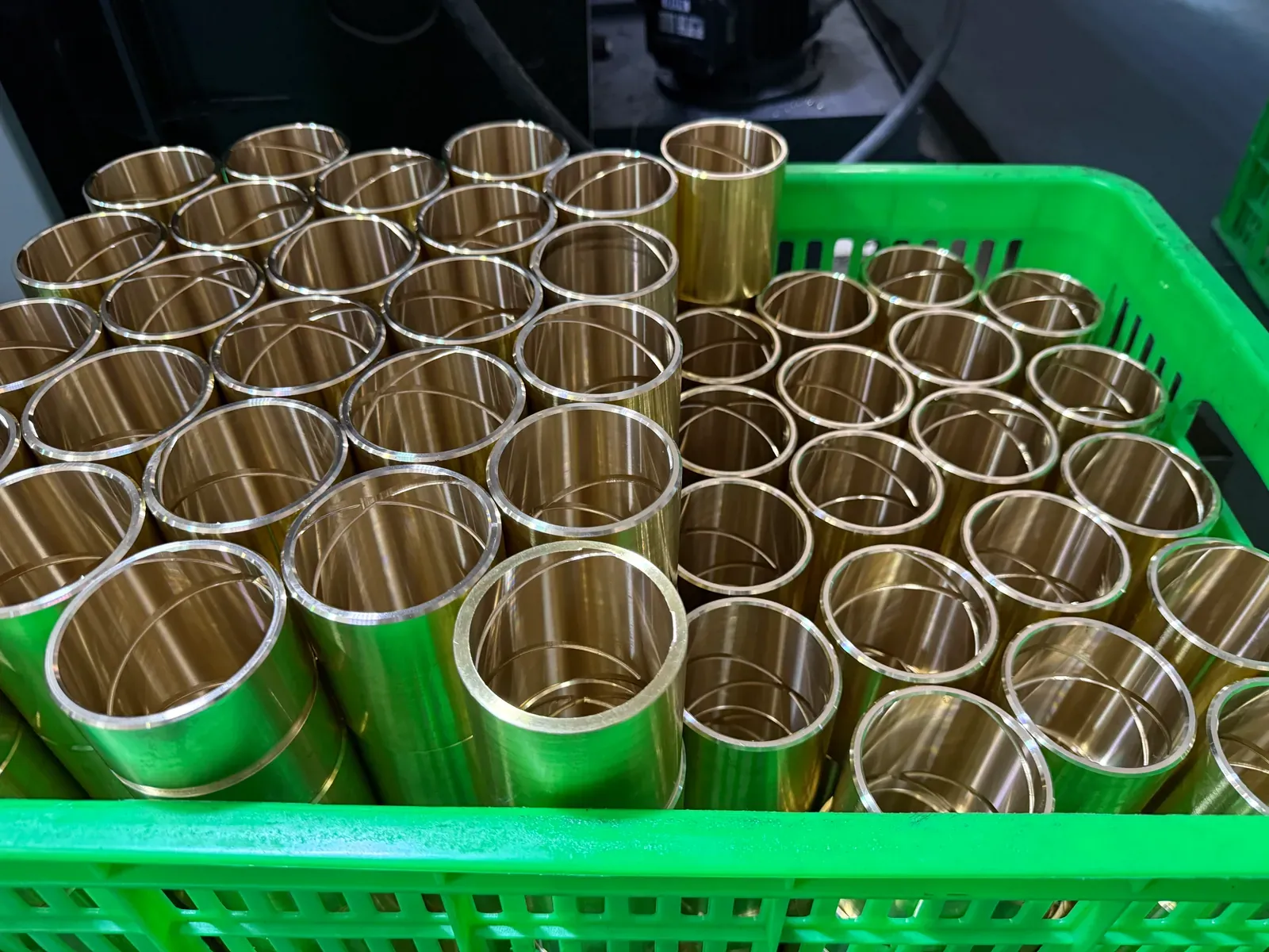 Machined cast bronze sleeve bushings of one size in a green basket, bright turned surfaces