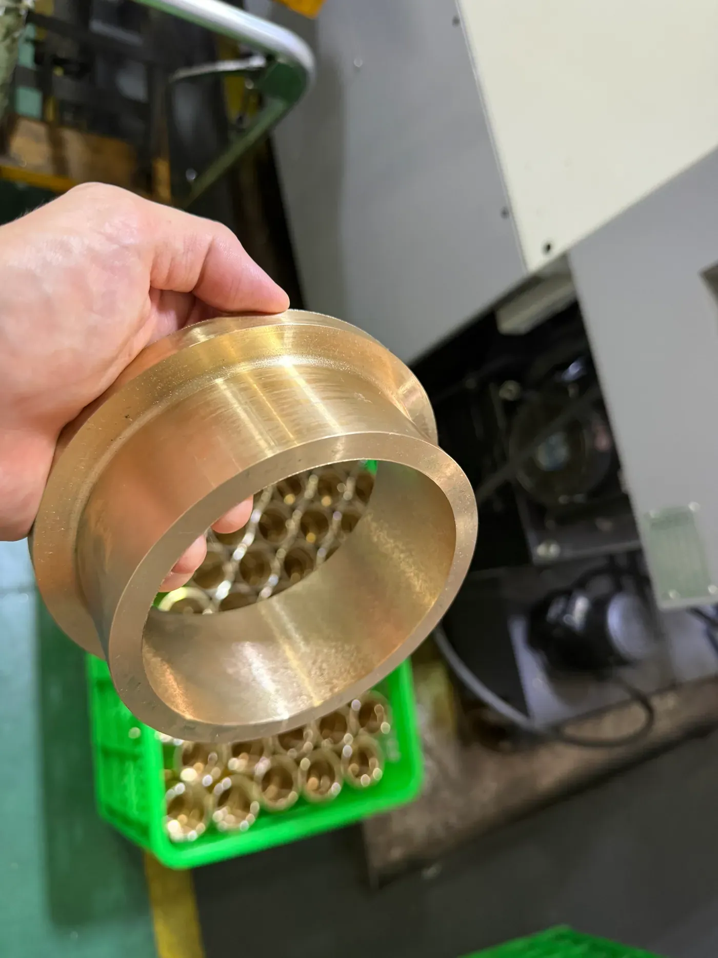 A large flanged cast bronze bushing held in one hand in the workshop